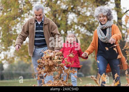 Les grands-parents et la petite-fille qui ont fait des coups de pied sur les feuilles d'automne dans le parc Banque D'Images