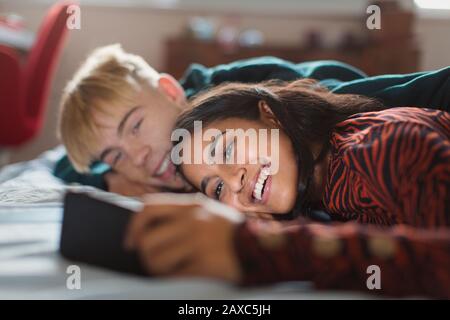 Couple d'adolescents souriants utilisant un smartphone sur le lit Banque D'Images