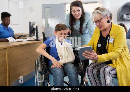 Médecin féminin avec tablette numérique parlant à la mère et aux enfants en fauteuil roulant dans le hall de la clinique Banque D'Images