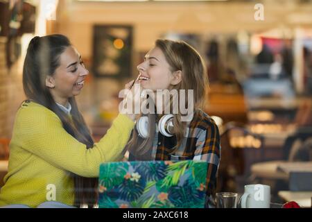 Jeune femme appliquant le brillant à lèvres d'amis dans la fenêtre de café Banque D'Images