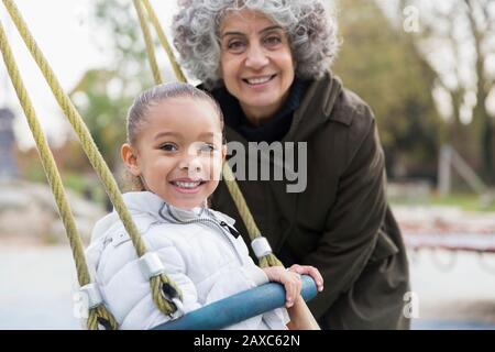 Portrait souriant grand-mère et petite-fille jouant sur l'oscillation à l'aire de jeux Banque D'Images