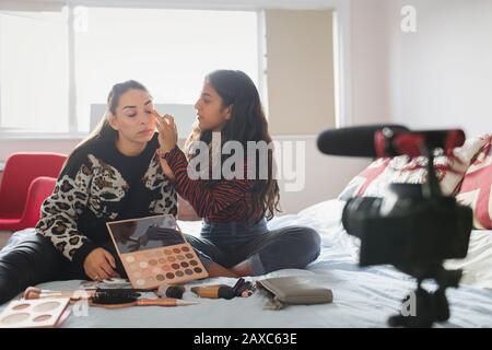 Les adolescentes se vantant d'une application de maquillage sur un lit dans la chambre Banque D'Images