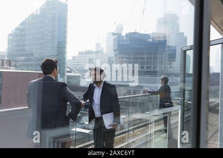 Les hommes d'affaires parlent sur un balcon de bureau ensoleillé et urbain Banque D'Images