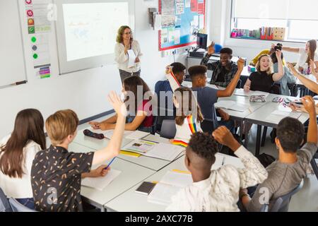 Élèves du secondaire avec les mains soulevées pendant la leçon en classe Banque D'Images