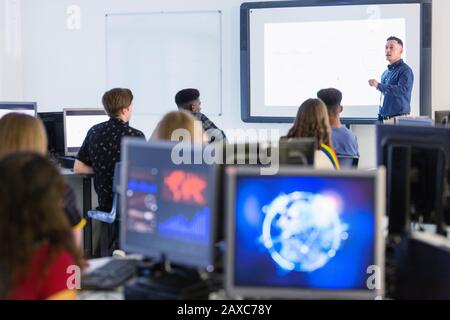 Jeunes élèves de haut niveau dans les ordinateurs regardant l'enseignant à l'écran de projection en classe Banque D'Images