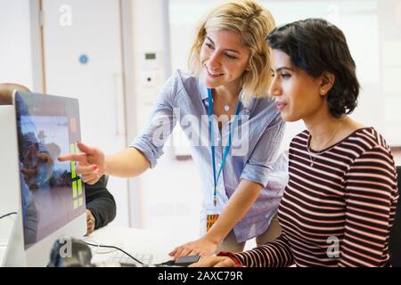 Professeur de photographie féminin aidant l'étudiant à l'ordinateur en classe Banque D'Images