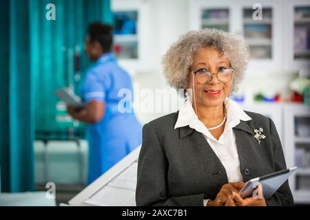 Portrait confiant médecin senior avec tablette numérique à l'hôpital Banque D'Images
