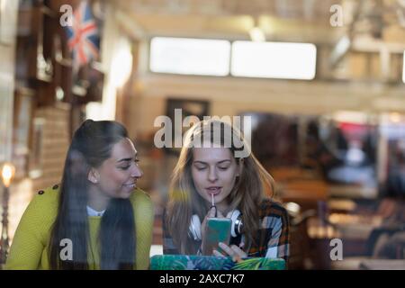 Jeunes femmes appliquant le brillant à lèvre dans la fenêtre de café Banque D'Images