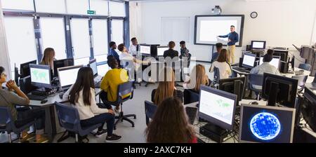 Jeunes étudiants utilisant des ordinateurs et regardant le professeur à l'écran de projection en salle de classe Banque D'Images