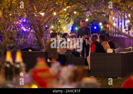 Les amis buvant sous les arbres avec des lumières à cordes à la fête du jardin Banque D'Images