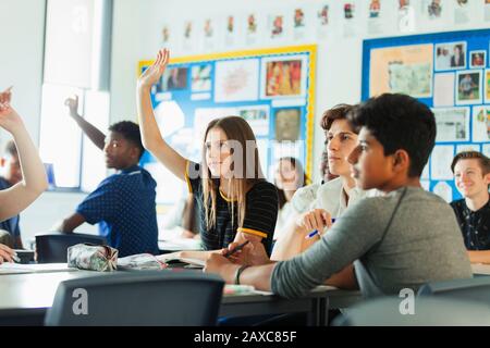 Élèves du secondaire ayant les mains soulevées, posant des questions pendant la leçon en classe Banque D'Images