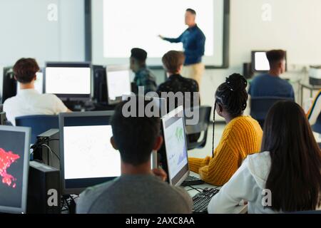 Jeunes élèves de haut niveau dans les ordinateurs regardant l'enseignant à l'écran de projection en classe Banque D'Images