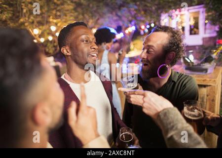 Des amis hommes heureux parlent et boivent à la fête du jardin Banque D'Images