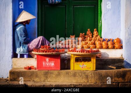 Vendeur de rue vietnamien portant un chapeau de paille traditionnel vendant des objets d'artisanat dans la rue à Hoi An Ancient Town, au centre du Vietnam. Banque D'Images