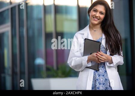 Belle brunette gaie étudiant ou stagiaire en médecine dentaire, psychiatrie, travail pharmaceutique, souriant avec une tablette électronique Banque D'Images