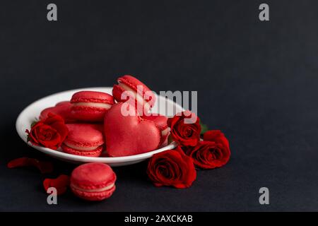 Délicieux macarons français avec des roses rouges sur fond noir. Concept pour la Saint-Valentin. Placer pour le texte. Banque D'Images