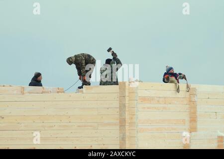 05.01.2020, Russie, Syktyvkar, les constructeurs de vêtements d'hiver construisent une maison en bois sur fond gris ciel nuageux. Saison d'hiver. Banque D'Images