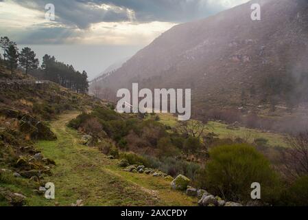 Sentier de montagne serpentant à travers une vallée brumeuse à Serra da Estrela, Portugal, pendant la lumière tôt le matin Banque D'Images