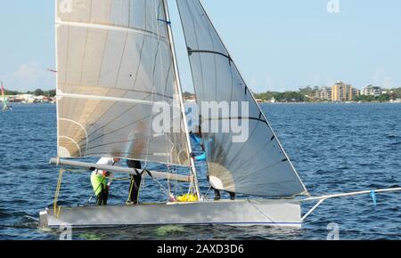 Les enfants naviguant sur un petit canot avec des voiles blanches s'approchent de près sur une voie navigable. Travail d'équipe par des marins juniors en course sur le lac d'eau salée Macquarie. Photo de Banque D'Images