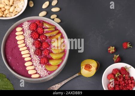 Bol à smoothie pour petit déjeuner sain avec prunes, framboises, arachides et graines de sésame sur fond sombre, photo horizontale, gros plan Banque D'Images