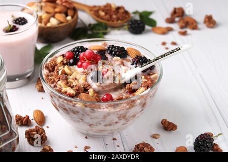 Muesli au miel croustillant de granola avec yaourt naturel, baies fraîches, chocolat et noix dans un bol sur fond clair, nourriture saine Banque D'Images