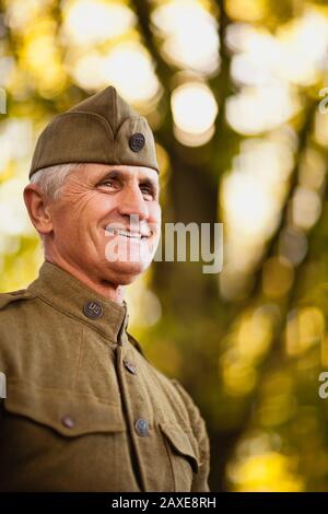 Le réacteur masculin mûr portant une casquette latérale et un uniforme de la seconde Guerre mondiale américain regarde et sourit comme il pose pour un portrait. Banque D'Images