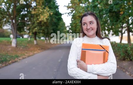 Belle écolière heureuse riant les sourires, les réjouissances, portrait d'été dans la rue de ville dans le parc, dans les mains des carnets de dossiers avec des manuels scolaires, au repos Banque D'Images