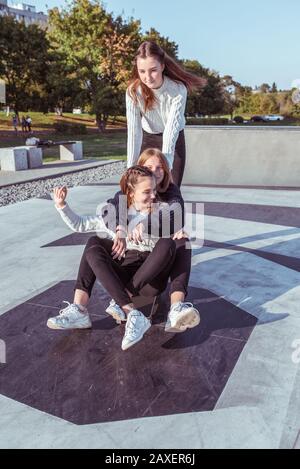 Trois adolescentes de 12 à 14 ans, en été en ville, skate board, souriant heureux, se réjouissant de plaisir. Week-end. Décontracté Banque D'Images