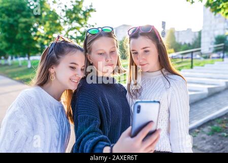 Trois adolescentes de 12 à 14 ans, ville d'été, smartphone main, souriant heureux, regarder des photos Internet. Selfie photo, en ligne. Décontracté Banque D'Images