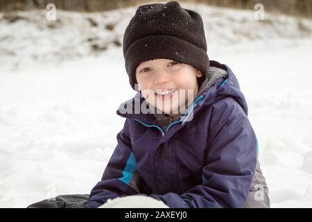 Winter Boy Smiling Assis Dans La Neige Banque D'Images