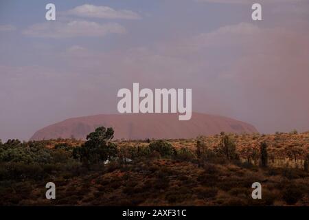 Un nuage de tempête de poussière rouge passe devant Uluru, le massif monolithe de grès dans le paysage désertique aride du « Red Centre » du territoire du Nord. Banque D'Images