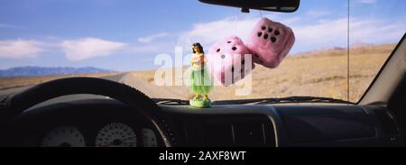 Des étaux flous pendus sur un rétroviseur avec une figurine de jeune fille hula sur le tableau de bord d'une voiture Banque D'Images