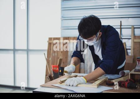 Homme asiatique Carpenter travaillant avec le dessin technique ou le papier de construction de photocalque reposant sur un atelier avec des outils de menuiserie et du bois à la maison Banque D'Images