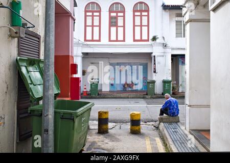 Vu d'une allée latérale étroite de Perak Road, Little India, Singapour, un homme est assis dans la rue entourée de vieux magasins chinois traditionnels Banque D'Images