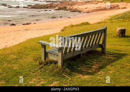 Banc de bois vert sur l'herbe à la plage surplombant les rochers Banque D'Images