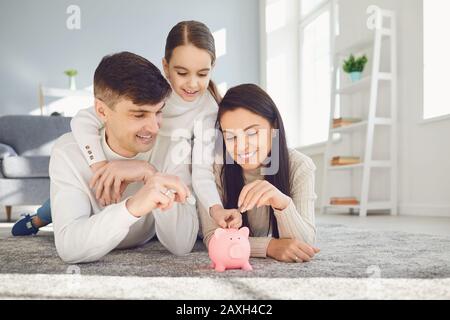 Une famille heureuse économise de l'argent dans un porc de banque piquante. Banque D'Images