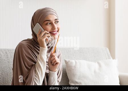 Arabe Fille Parler Sur Cellphone À La Maison Avec Crayon Près Du Visage Banque D'Images