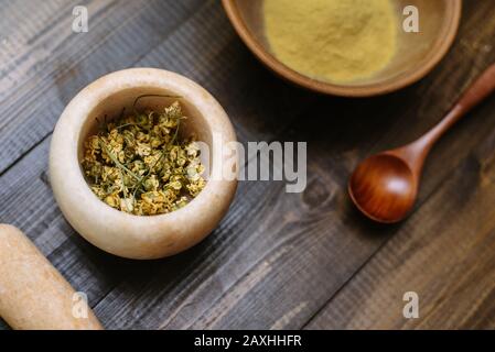 Mortier de marbre avec camomille séchée pour cosmétiques naturels. Bol en argile avec poudre jaune ou argile et fleurs sur fond en bois. Pose plate. Banque D'Images