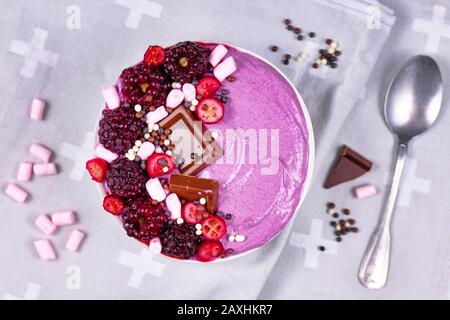 Bol à smoothie aux fruits décoré de framboises rouges saines, de canneberges, de petits marshmallows et de morceaux de chocolat Banque D'Images