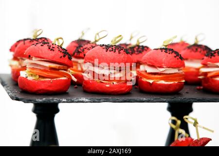 Petits hamburgers avec pain rouge, farcis de jambon et de tomate, saupoudrés de graines de sésame noir Banque D'Images