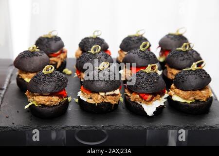 Petits hamburgers avec pain noir, farcis de bœuf et de tomate, saupoudrés de graines de sésame noir Banque D'Images