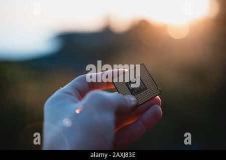 Personne tenant un processeur d'ordinateur à l'extérieur au coucher du soleil. Point de vue tourné. Concept de CPU. Banque D'Images