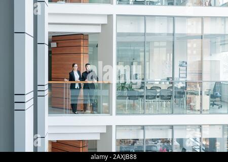Les jeunes employés du centre d'affaires se tenant à la rampe et regardant autour, l'intérieur de la salle de bureau glassy Banque D'Images