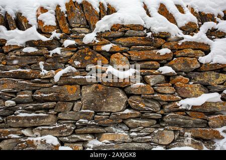 Maçonnerie ancienne recouverte de neige comme fond ou texture. Fragment d'un mur de pierre. France, Alpes Banque D'Images