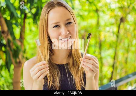 La jeune femme tient une brosse à dents en bambou sur un fond de bambou vert croissant Banque D'Images