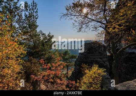 Suisse saxonne en automne. Soleil avec un ciel bleu à travers les arbres avec des rochers et une vue du pont de Bastei sur la vallée dans la pierre de l'Elbe Banque D'Images