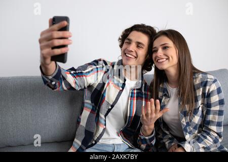 Jeune couple souriant prenant selfie sur le canapé. Banque D'Images