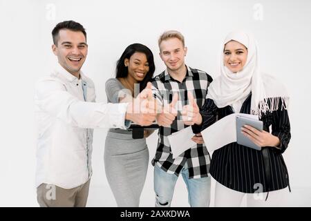 Groupe de quatre étudiants multiraciaux ou partenaires commerciaux, des femmes musulmanes et africaines, deux hommes caucasiens, souriant et debout ensemble, montrant leur Banque D'Images
