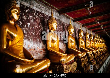 Gros plan d'une truelle de statues de Bouddha d'or le long d'un mur. Banque D'Images