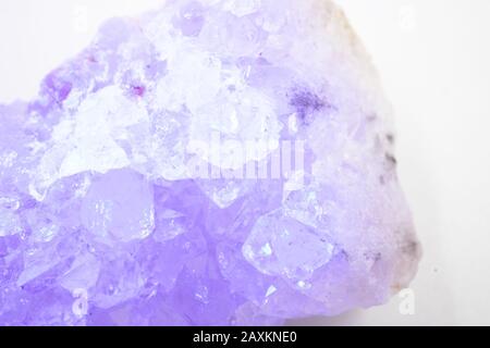 Gros plan d'une pierre en cristal avec couleur lilas contre un arrière-plan blanc Banque D'Images